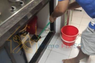 A plumber using specialized tools to clean a clogged kitchen drainage pipe under a sink area.