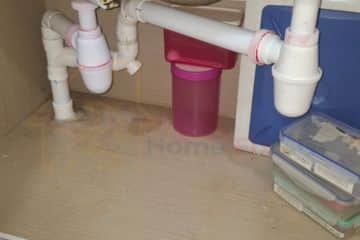 A close-up view of a white PVC drainage pipe system and P-traps installed under a sink inside a wooden cabinet.