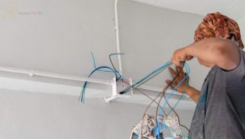 A licensed electrician installing new electrical wiring and PVC conduits into a junction box on a white wall in a Singapore HDB apartment.
